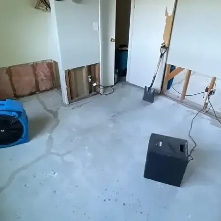 Air movers and dehumidifier drying a room with lower drywall removed and bare floor