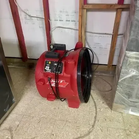 Red air mover drying a room with the lower wall opened and plastic sheeting hung
