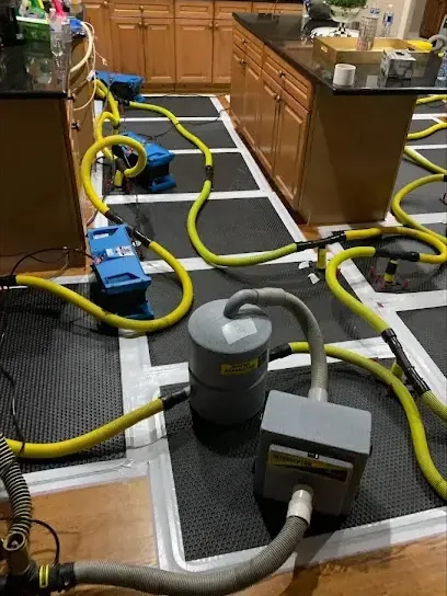 Drying mats and hoses laid over a kitchen hardwood floor during structural drying